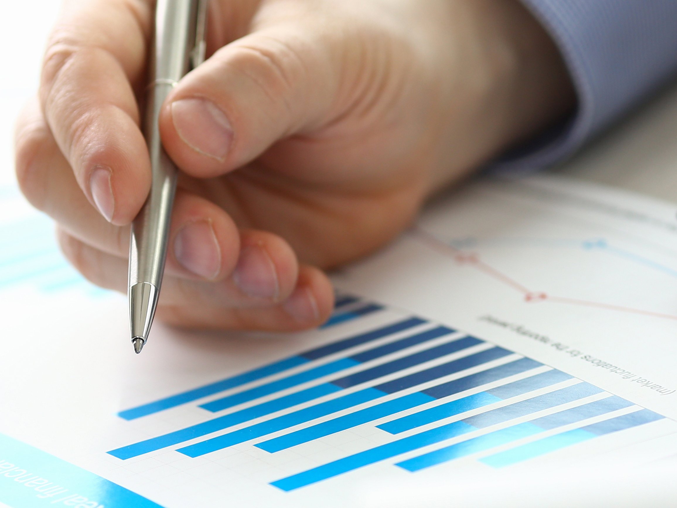 Eine Person schreibt etwas auf ein ausgedrucktem Balken-Diagramm. Daneben ist ein Taschenrechner zu sehen.